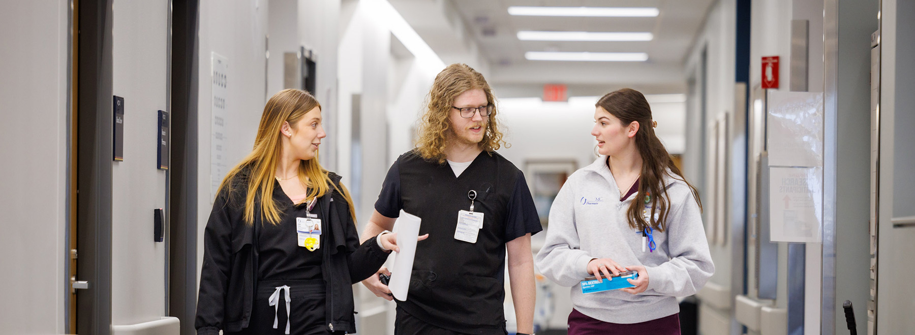 Three pharmacy residents converse while walking down a hospital corridor.