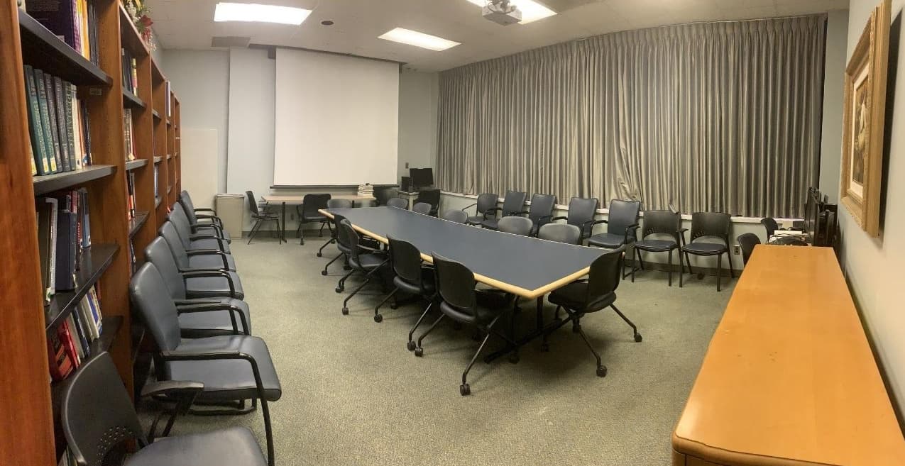 A large conference room features a long conference table with chairs and additional chair around the perimeter of the room.