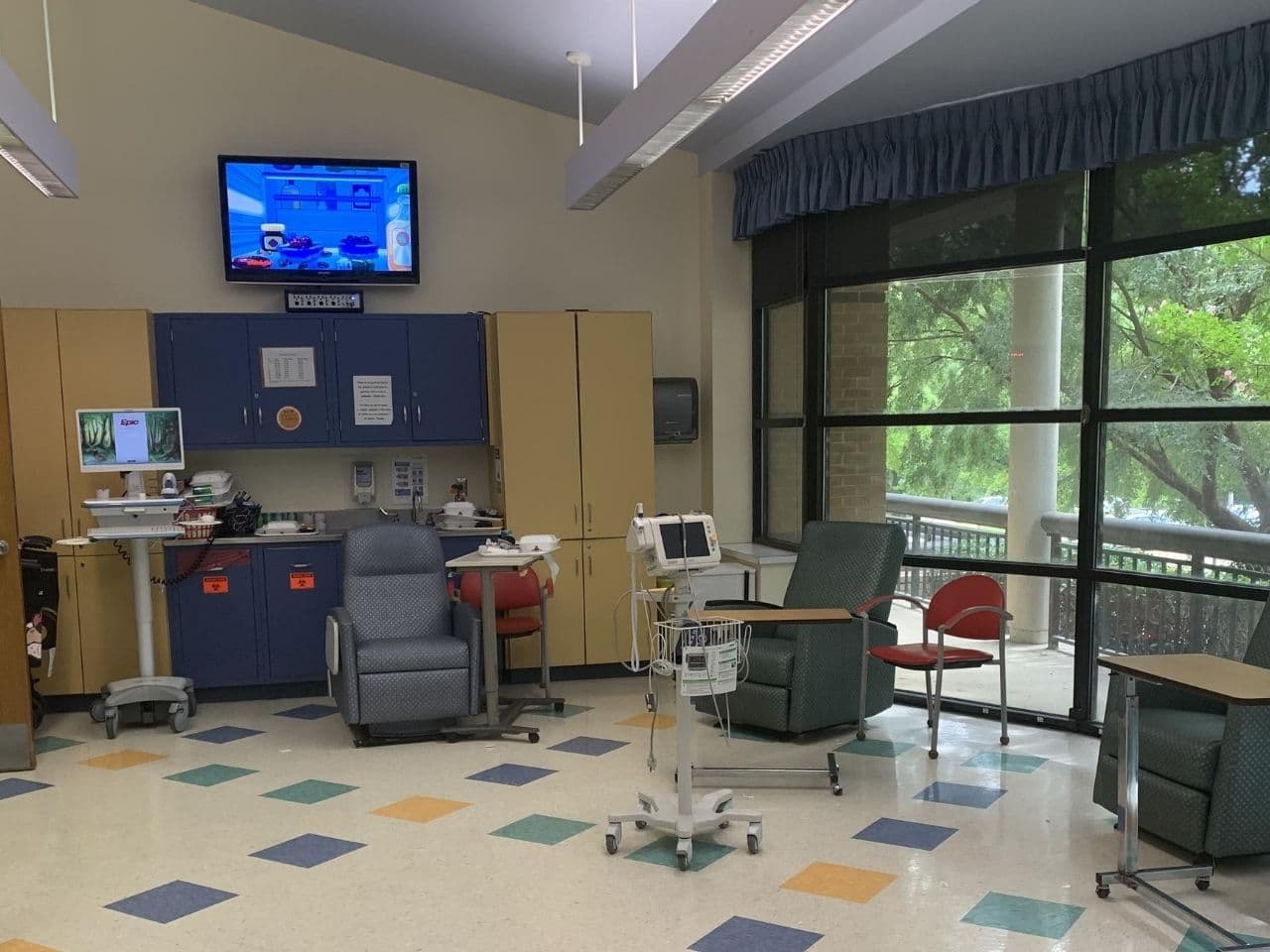 The infusion area has big windows that let in lots of natural light; colorful tiles on the floor, a flatscreen TV mounted on the wall, and several infusion recliners.