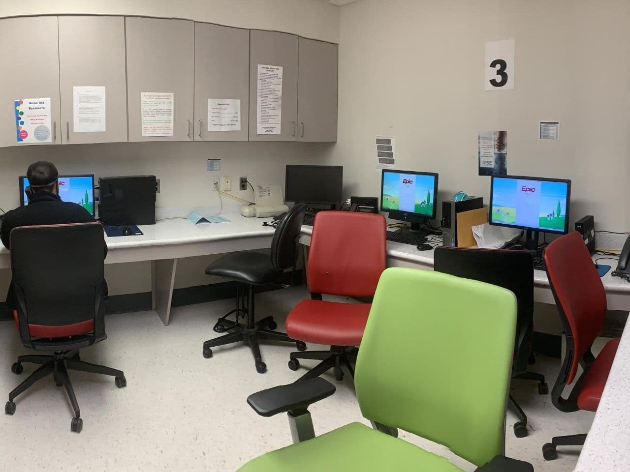A doctor's room has multiple computer stations, chair, and storage cabinets.