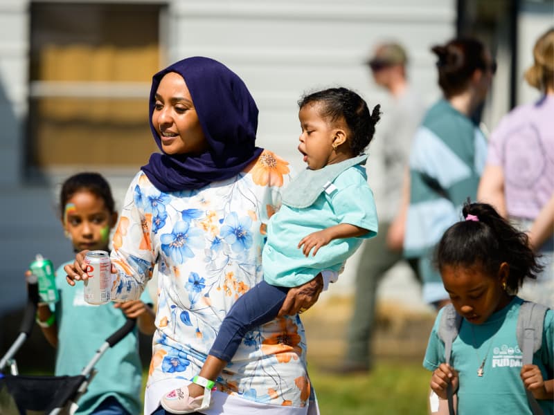 A woman holds a child and walks with two other children, enjoying time together at Family Fun Day 2026.