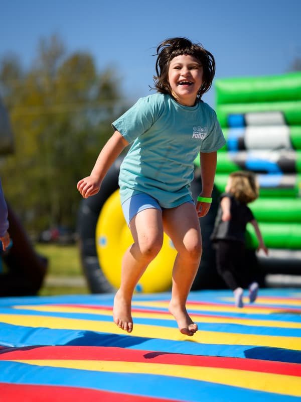 A barefoot girl smiles as she jumps on a bouncy toy at Family Fun Day 2026.