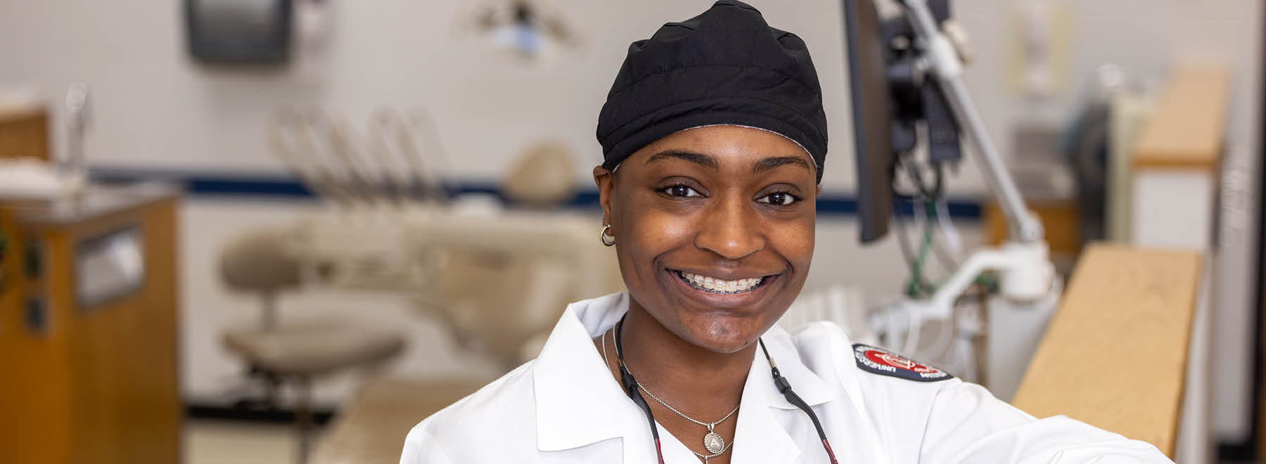 A smiling young woman in a UMMC lab coat poses in a dental office setting.