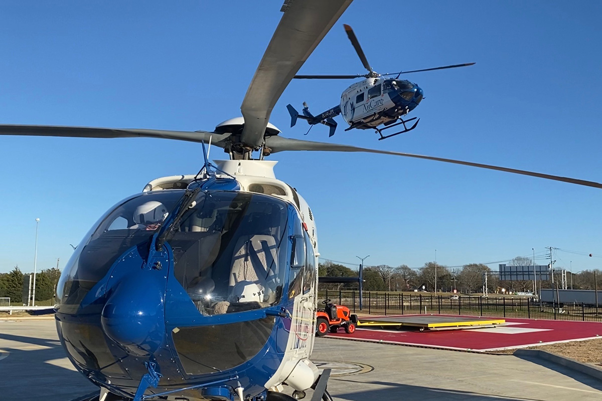 Two AIrCare helicopters at the launchpad with one in flight.