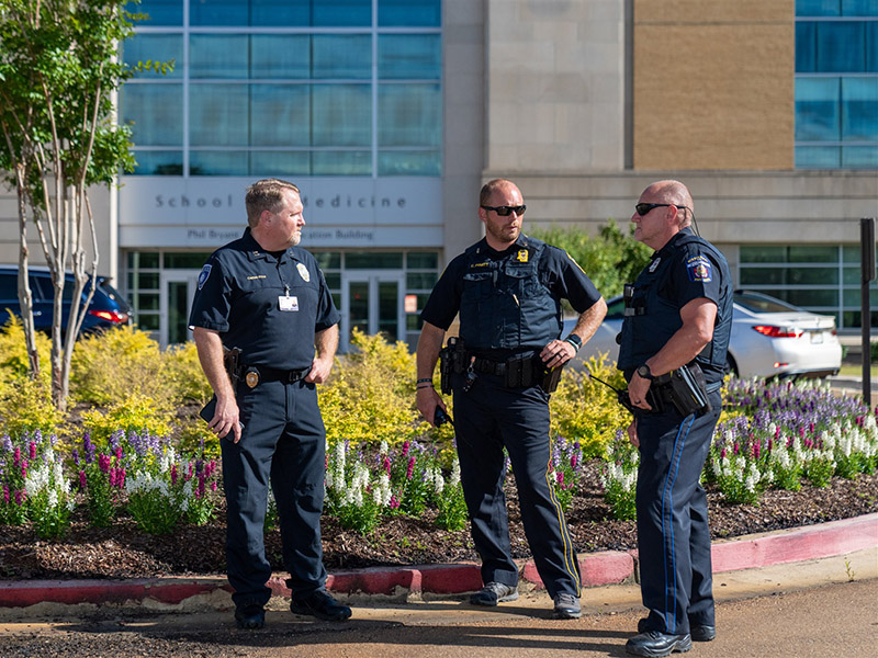 Three UMMC police officers standing in front of the landscaping at the School of Medicine.