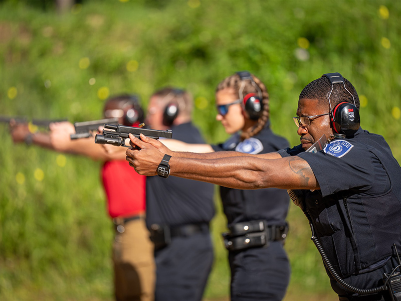 Four UMMC police officers at gun practice outdoors with the fourth one in focus.