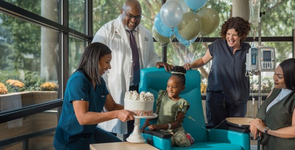 Young patient smiles when presented with birthday cake by doctors and nurses.