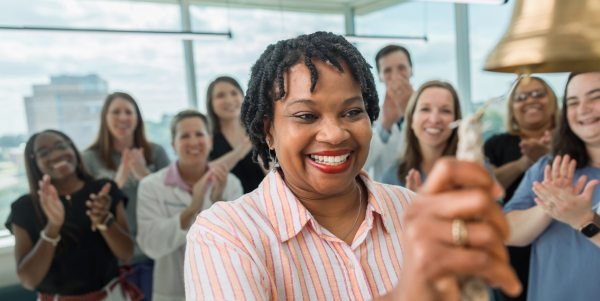 Smiling patient rings bell while others clap in background.