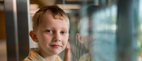 Child leans against glass partition with reflection clearly visible.