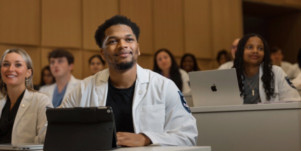 Student sitting in classroom listens to lecture while smiling.