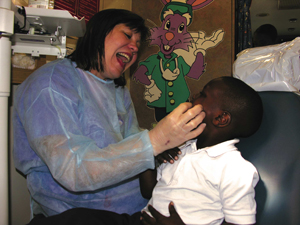 Dr. Neva Eklund, associate professor and department chair of pediatric and public health dentistry in the School of Dentistry, shows 4-year-old Jaylin Garrison how wide he should open his mouth for an oral screening at Smith Elementary School.