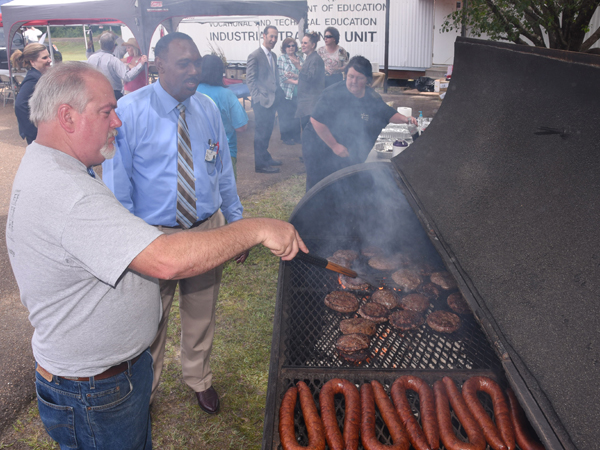 As UMMC Holmes County and Grenada director of ambulatory operations Dewery Montgomery looks on, Jeremy Adcock (left), UMMC Holmes County manager of support services, flips burgers and monitors sausage.