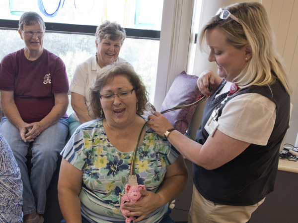 Debbie Davis of Williamsville Baptist Church hugs a piglet-themed crocheted telemetry bag designed to hold a heart monitor. Looking on is hospital school educator Luellen McPhail, right.