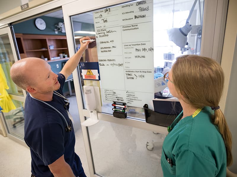 Dale Brewer, left, R.N., and Laura Stevens, R.N., review patient information on a communication board in the Cardiac Intensive Care Unit. The Joint Commission gave the adult critical care units kudos for their use of the boards.