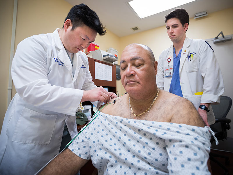 Dr. Hyung Kim, left, assistant professor of neurosurgery, attaches electrical leads to acupuncture needles in patient John Keys' shoulders while Seth Knight, right, a third-year medical student, looks on during a treatment at the G. V. 