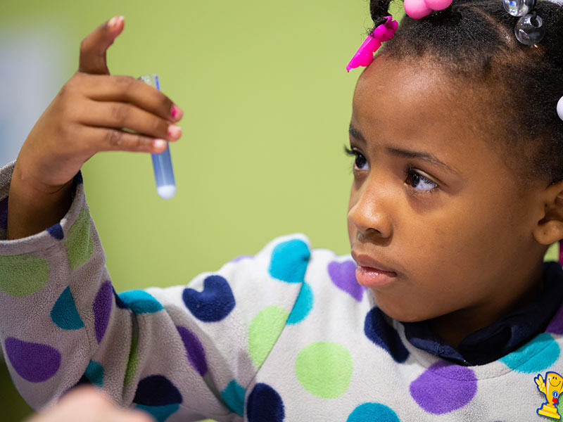 NAME, a kindergarten student at Pecan Park Elementary, watches her purple solution turn blue, showing how antacids neutralize acid.