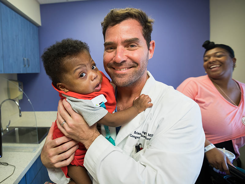 Dr. Brian Kogon holds Faust with the Medical Center's youngest heart transplant patient's mom, Candace, looking on.