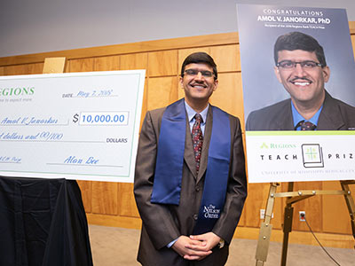 Janorkar, the 2018 Regions TEACH Prize winner, is framed by a ceremonial check and a congratulatory poster.