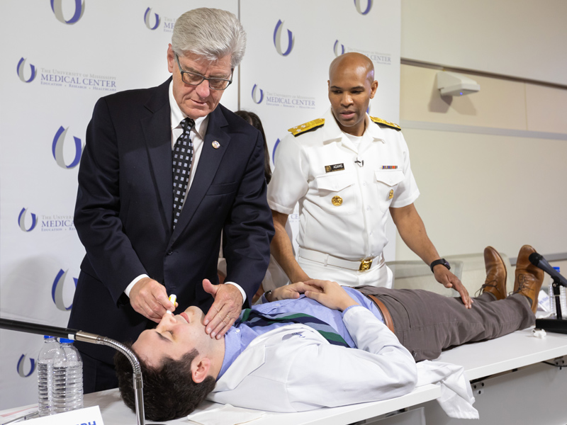 US. Surgeon General Jerome Adams, right, instructs Mississippi Gov. Phil Bryant on how to administrate the opioid-reversal drug naloxone to Dr. John Caleb Grenn, internal medicine and pediatrics resident.