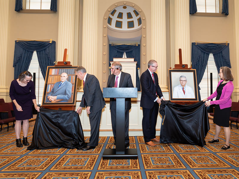 Kane Ditto, at podium, oversees the unveiling of the portraits of Dr. Arthur Guyton, left, beside Dr. Jean Gispen and Dr. John Hall, and Dr. James Hardy beside Dr. Chris Anderson and Dr. Bettie Winn Hardy Story.