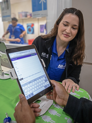 Hands in foreground holding tablet with survey questions as woman in background looks on.