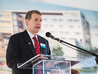 Guy Giesecke behind clear podium speaking at ground-breaking ceremony for pediatric expansion.