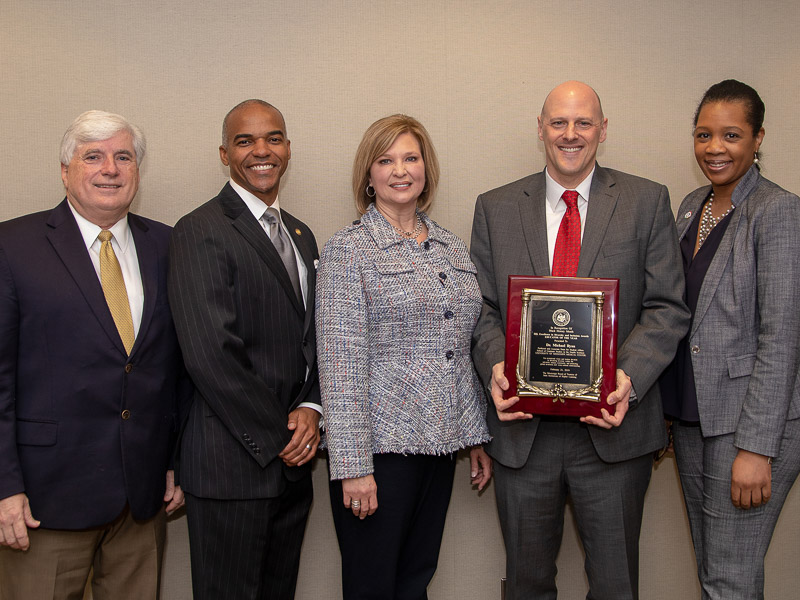 Dr. Mike Ryan holding his award posing with Dr. Joey Granger, UMMC dean of the School for Graduate Studies in the Health Sciences; Dr. Steven Cunningham, IHL board of trustees; Dr. LouAnn Woodward, UMMC vice chancellor; Dr. Juanyce Taylor, UMMC chief diversity and inclusion officer.