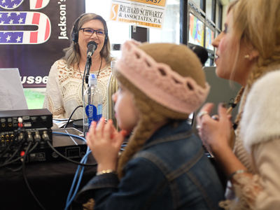 Woman talking into microphone while child and mother, in foreground, are interviewed.