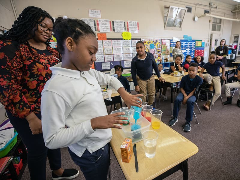 Barack H. Obama Magnet student Amerie Thomas, 10, mixes colorful volcanoes using vinegar, baking soda and food dye under the watch of SGSHS student Adesuwa Ekunwe as part of Project REACH, an education partnership between UMMC and the elementary school.