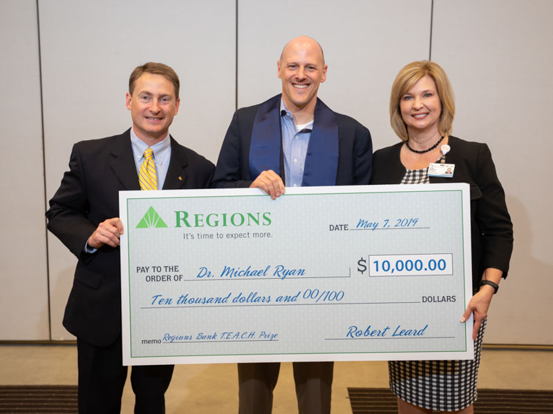 Dr. Michael Ryan, center, received the 2019 Regions TEACH (Toward Educational Advancement in Care and Health) Prize May 7 at UMMC. Robert Leard, market executive for Regions Bank, left, and Dr. LouAnn Woodward, UMMC vice chancellor for health affairs, presented him with the award.