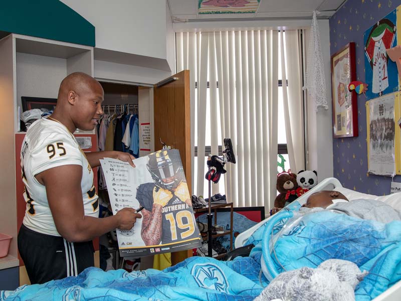 Southern Miss defensive lineman Andrew Cole delivers a Golden Eagles poster to Batson Children's Hospital patient Will Currie.
