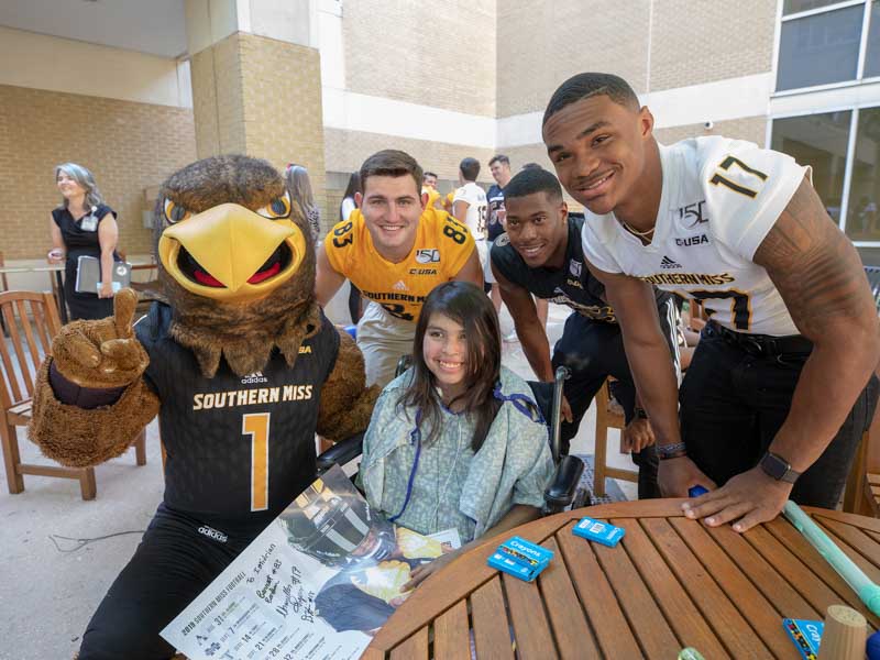 University of Southern Mississippi mascot Seymour and football players, from left, wide receiver Barrett Barham, wide receiver De'Michael Harris and quarterback Chandler Rogers smile with patient Imidrian York of Heidelberg.