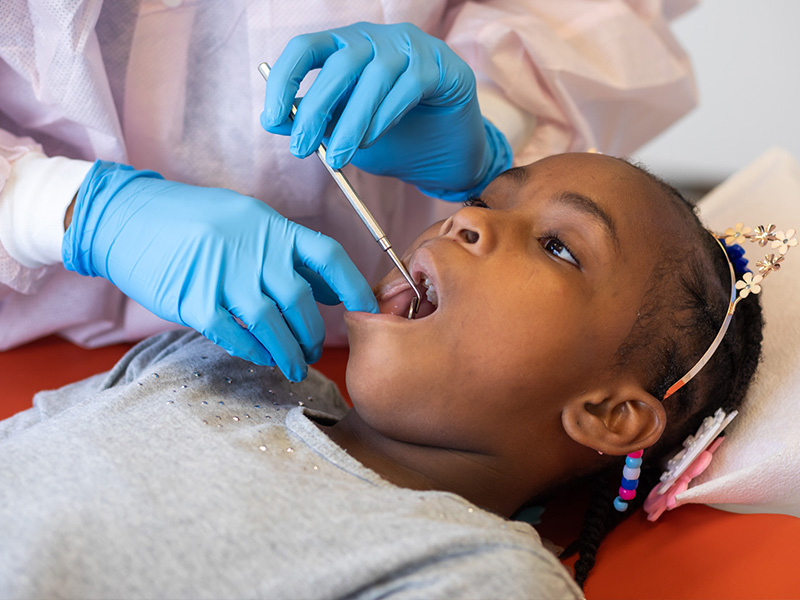 Marsha Jones stares out the panoramic in the pediatric dentistry clinic windows while Koti does an examination of her teeth.