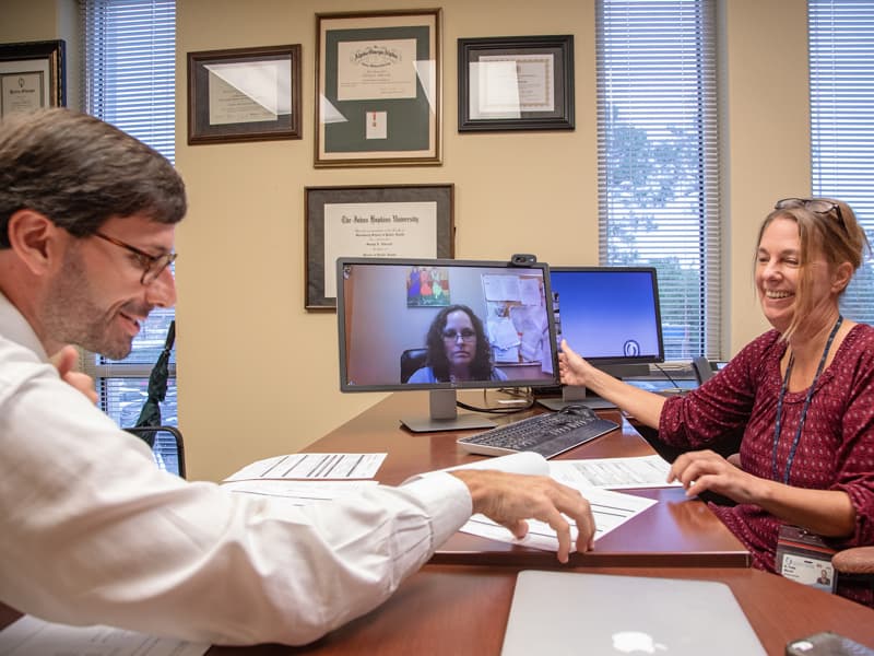 Dr. Svenja Albrecht, right, scans a patient record as Darryl Adams, nurse practitioner on screen, discusses the patient's Hepatitis C. Joining them is Peyton Harrington, a clinical pharmacy specialist.