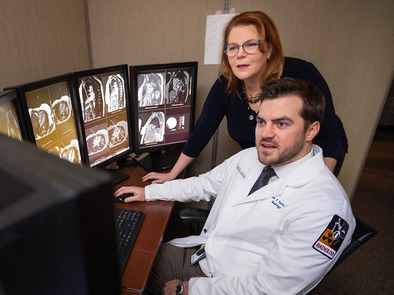 Two radiologists look at scans on computer screens.