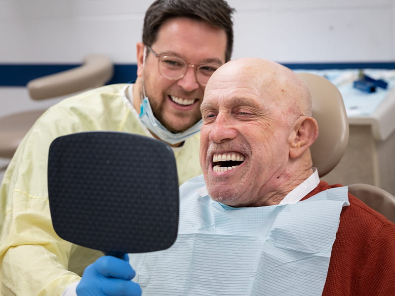 A dental student watches while a patient enjoys inspecting his new dentures.