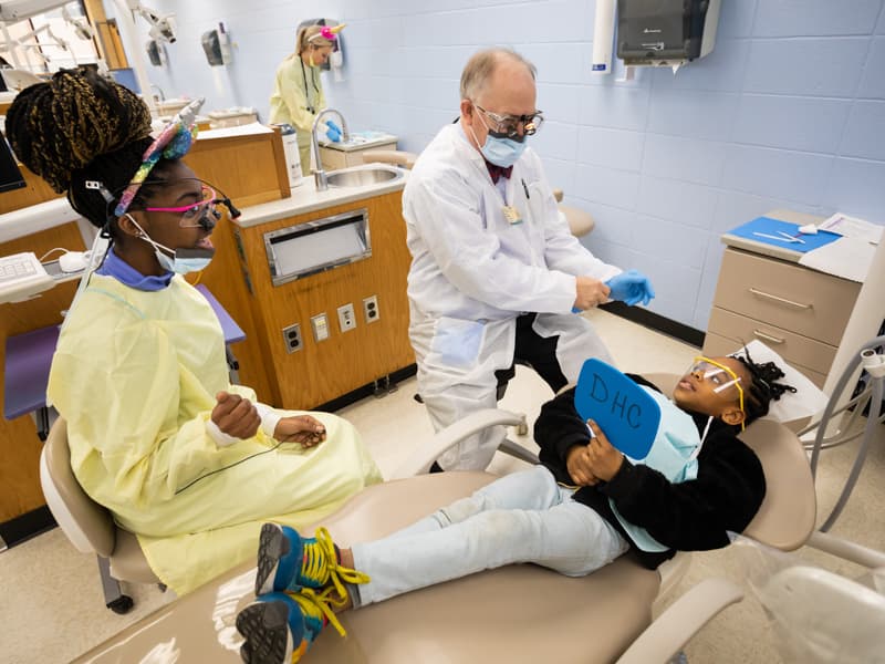 Dental student looks on as her professor checks out a pediatric patient.