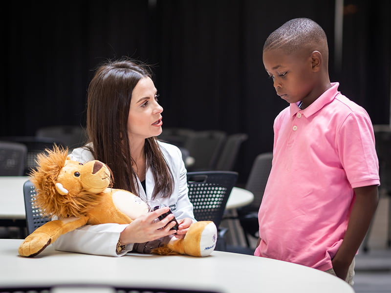 A doctor shows a pediatric patient how to use an insulin pump with the help of a stuffed lion.