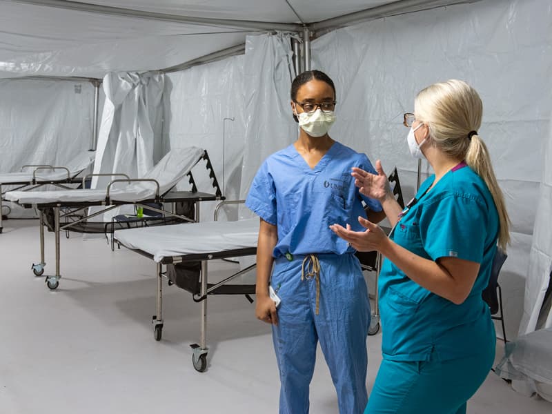Licensed practical nurse Policia Travis, left, and nurse manager Ashley Gustafson finish preparations for patients to arrive at a temporary field hospital in Garage B.