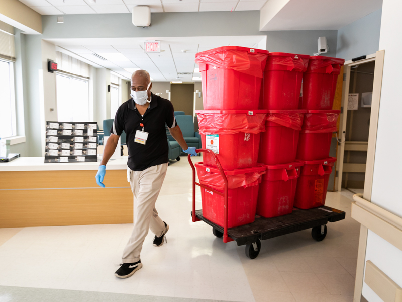 Housekeeper Bill Culpepper pulls a dolly laden with nine hazardous waste containers holding soiled and contaminated personal protective equipment and medical supplies from the medical ICU.