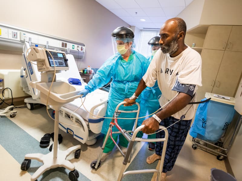 Gretta Harvey, left, physical therapist, and Annice Nelson, background, occupational therapist, help Lajarvis Travis walk to the sink in his room on 2 North.