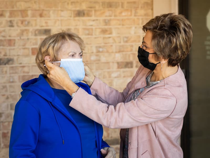 Darlene Bryant, right, helps her mother, Bonnie Acey, with her mask during a recent visit at an assisted living facility.
