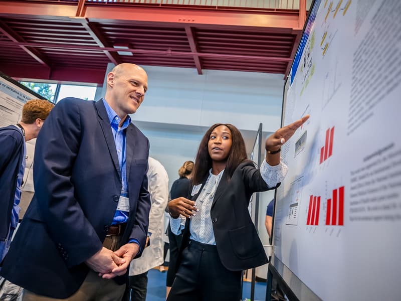 Dr. Michael Ryan listens to Kristen Smith, SURE student in the Department of Pharmacology and Toxicology, during the 2019 Summer Undergraduate Research Symposium.