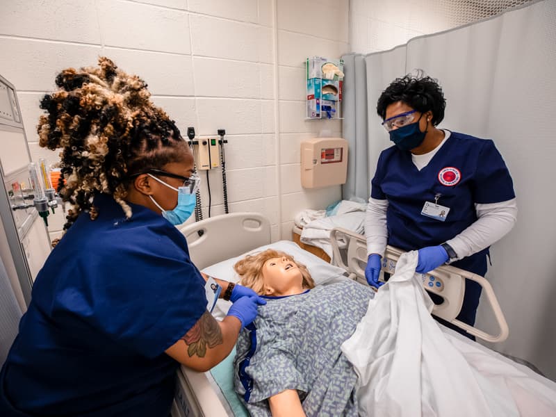 During their first week in the Accelerated BSN program, Asia Madison, left, and Erica Logan practice tucking a mannequin 