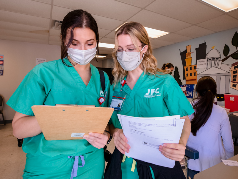 School of Medicine students Reagan Moak, left, and Rachael Pace check to see who's next in line for a COVID-19 vaccine Saturday at the Jackson Free Clinic.