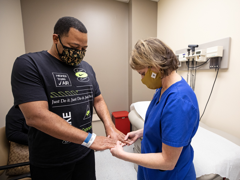 Occupational therapist Amy Mayhue checks the circulation in COVID-19 survivor Derek Carter's fingers during his recent visit to the ICU Recovery Clinic.