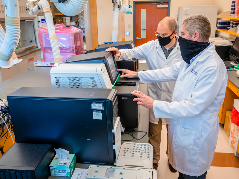 Dr. Ashley Robinson, back, and Dr. Michael Garrett, front, UMMC scientists, prepare COVID-19 samples for genomic sequencing, a tool that allows researchers to distinguish between virus variants to determine which are more or less prevalent in the population.