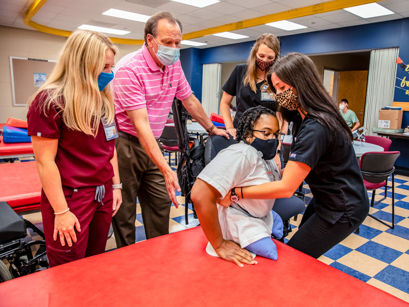 Baylee Bryant, right, and occupational therapy classmate Miracle Buckley practice transferring a patient from a wheelchair while from left, Kaitlin Wallace, Dr. Peter Giroux, and Abbie Scott look on.