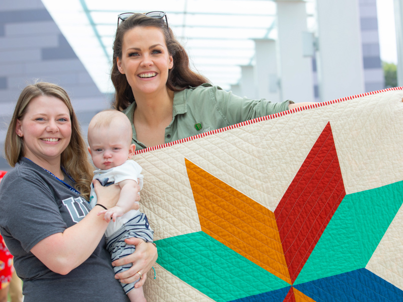 Girl Scout Troop 3965 leader Jessica Dowdy holds a baby quilt she made for Evan Johnson, held by mom Ashley Johnson, a research scientist at UMMC. Evan's stay in neonatal intensive care inspired the Girl Scout troop to make quilts for babies in the NICU at the Kathy and Joe Sanderson Tower at Children's of Mississippi.