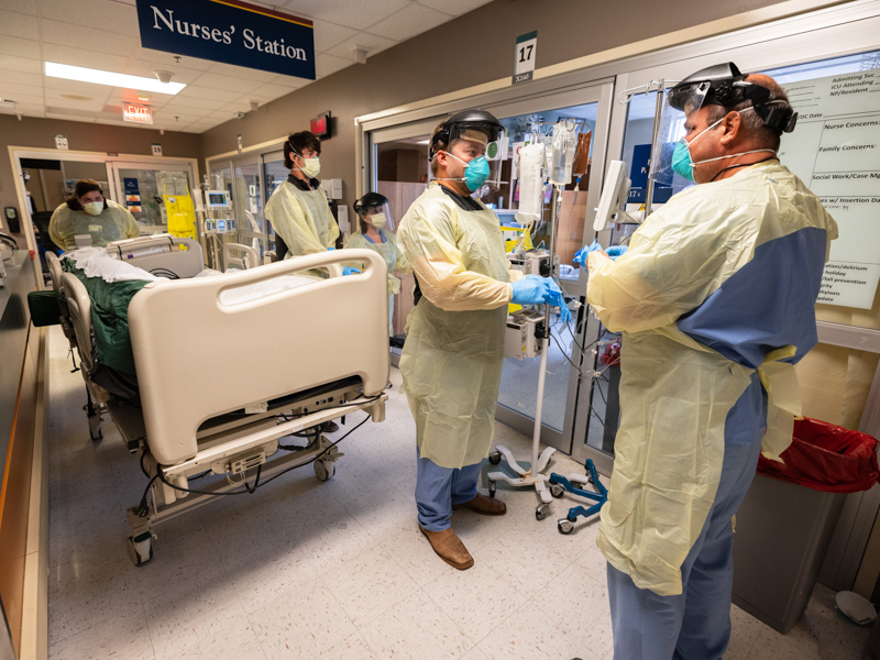 Medical Intensive Care Unit registered nurses Matt Harris, center, and Steve Donnell, right, join a team preparing to move a COVID-positive patient into a new bed August 11.